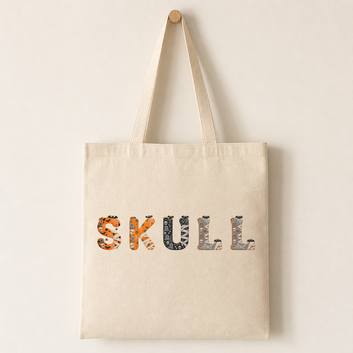 Plain canvas tote printed across the front with several Skeleton Spooks characters, showing bats perched above and corner icons like spiders and tiny tombstones.