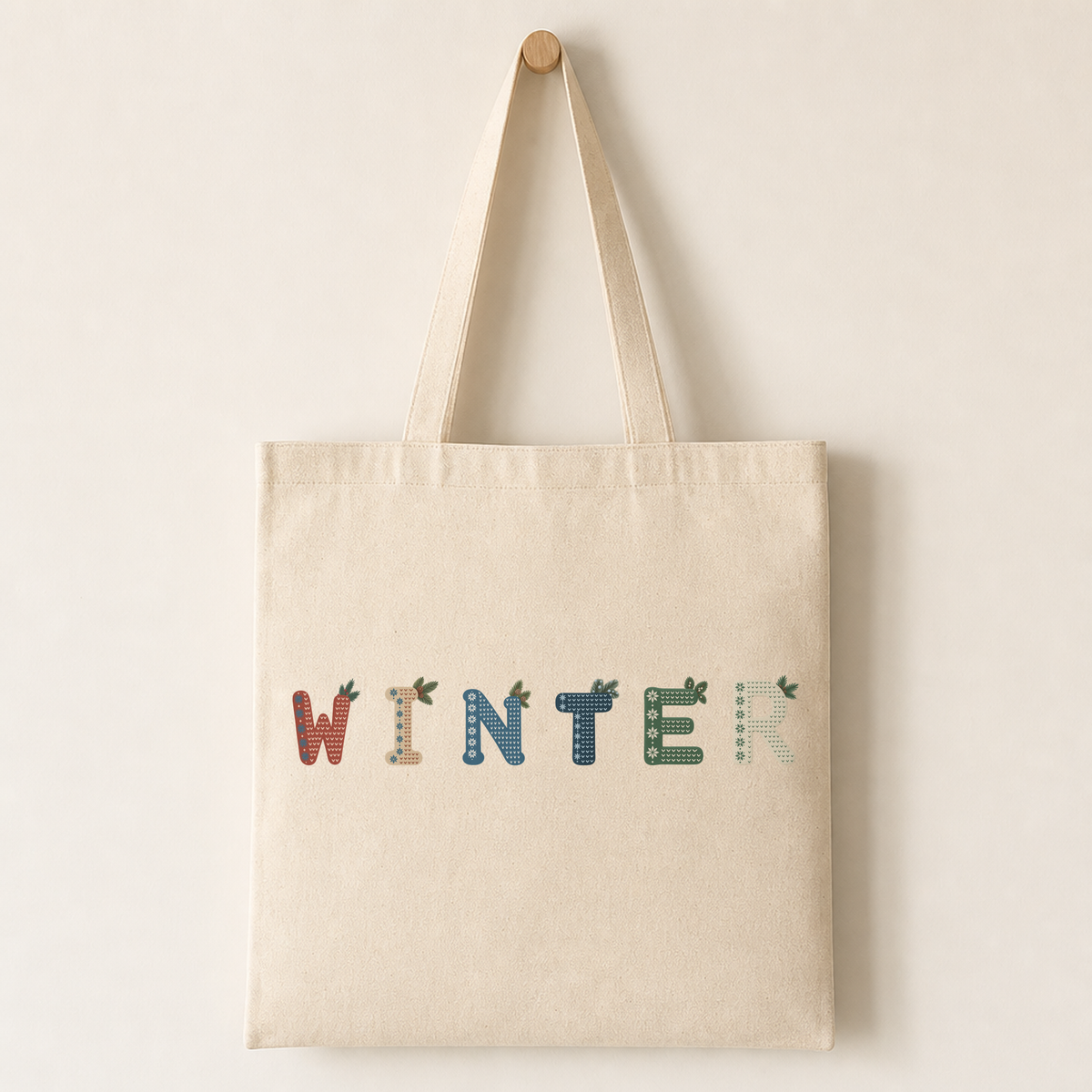 Canvas tote bag printed with a Nordic Winter letter featuring the snowflake band, knitted chevron texture and pine sprigs