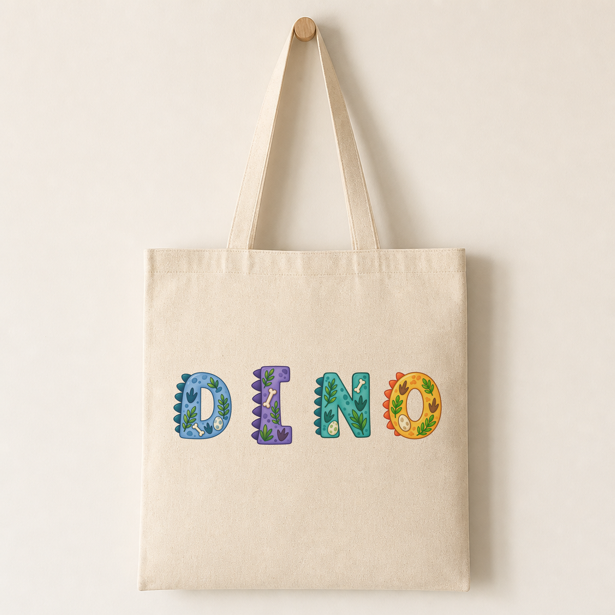 Canvas tote bag printed with a dinosaur letter design positioned centre-left on the bag.