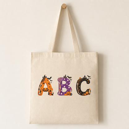 Plain canvas tote bag with several Mina characters printed across the front, including the mini pumpkins and candle detail at the bottom-right.