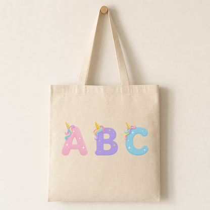A canvas tote bag printed with a unicorn letter centred on the front, showing the gold horn, pastel mane and sparkles.