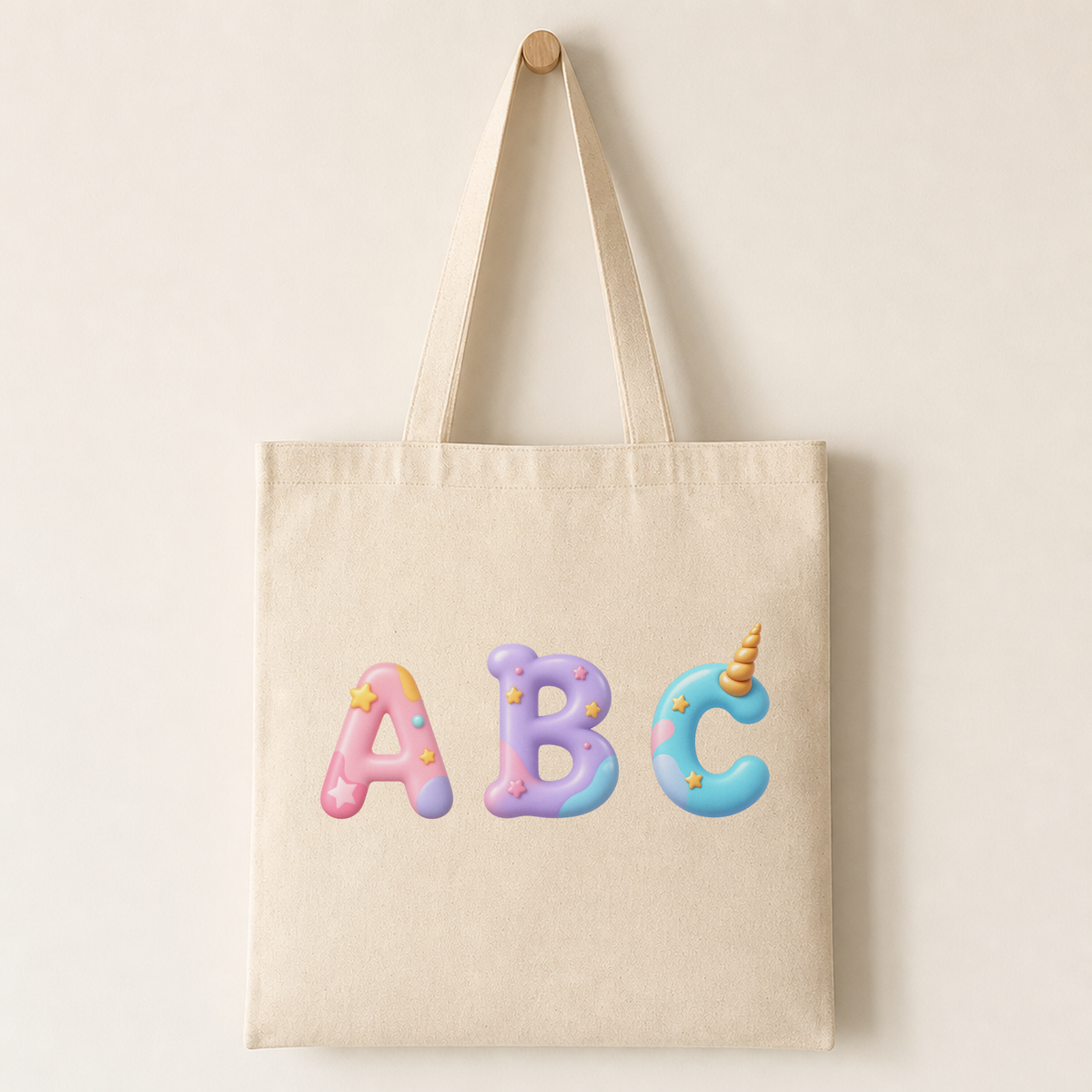 Natural canvas tote bag printed with a unicorn-themed capital letter featuring a gold horn, pastel mane and small star sparkles as a product mock-up.