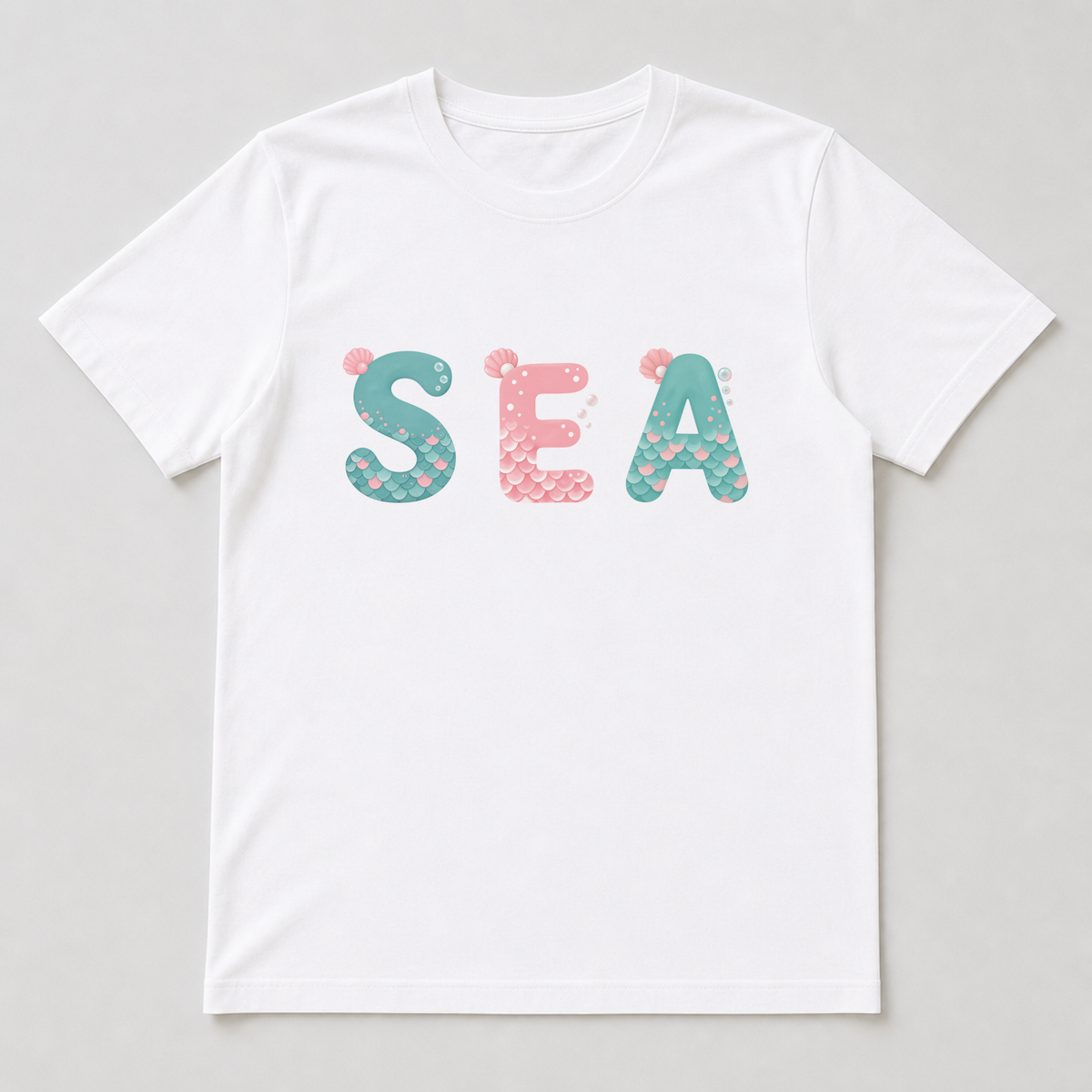 White t-shirt mockup showing a mermaid alphabet letter printed on the chest with scallop-shaped scales, a pink shell and tiny bubbles.