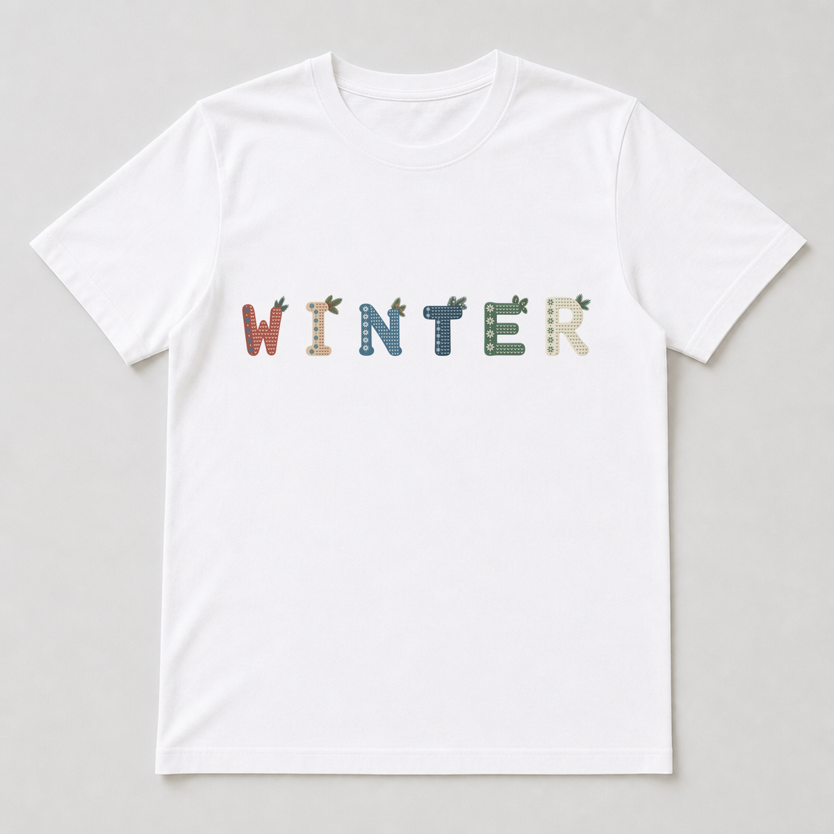 White t-shirt printed with a single Nordic Winter letter showing the left snowflake band and top-right pine sprigs