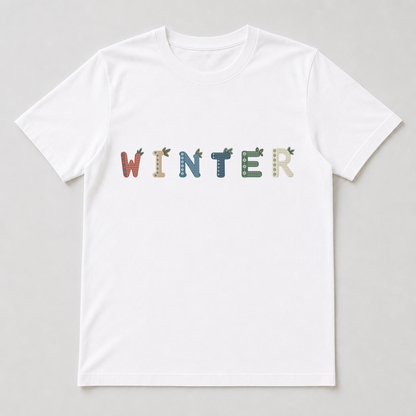 White t-shirt printed with a single Nordic Winter letter showing the left snowflake band and top-right pine sprigs